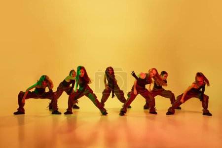 Foto de Baile de contemporáneos, hip-hop. Grupo de niñas, niños, en ropa deportiva con estilo bailando sobre fondo de estudio amarillo en luz de neón. Concepto de infancia, afición, estilo de vida deportivo - Imagen libre de derechos