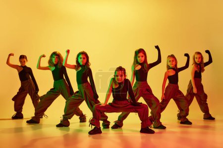 Modern style. Group of talented kids, autistic children in stylish clothes dancing, performing hip-hop against yellow studio background in neon light. Concept of childhood, hobby, sportive lifestyle