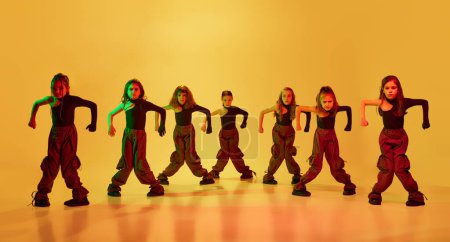 Photo for Group of artistic, little dancers, girls, children in stylish sportive clothes dancing hip-hop against yellow studio background in neon light. Concept of childhood, hobby, sportive lifestyle - Royalty Free Image