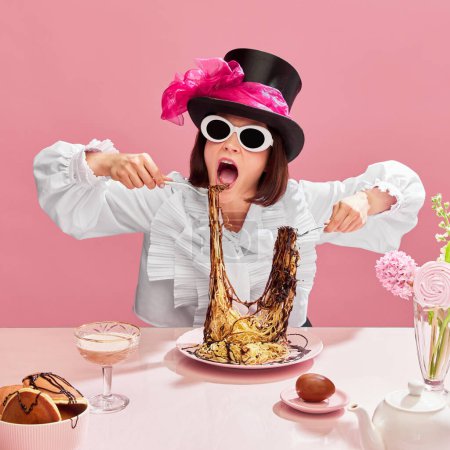 Téléchargez les photos : Mangeur passionné. Femme émotionnelle en chapeau cylindrique et lunettes de soleil mangeant des spaghettis avec sauce au chocolat sur fond rose. Gourmet. Concept de pop art, créativité, nourriture, inspiration, émotions - en image libre de droit