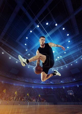 Photo for Dynamic image of young man, professional basketball player in motion, jumping with ball during match on 3D stadium with flashlights. Concept of professional sport, competition, action and motion - Royalty Free Image
