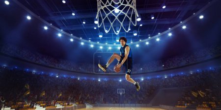 Photo for Young man, professional basketball player in motion, jumping with ball during match on 3D stadium with flashlights. Winning game. Concept of professional sport, competition, action and motion - Royalty Free Image