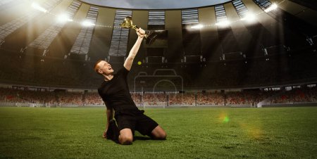 Photo for Young happy man, professional sportsman in black uniform sitting on knees on 3D field with trophy after winning championship. Concept of sport, competition, game, emotions, success - Royalty Free Image