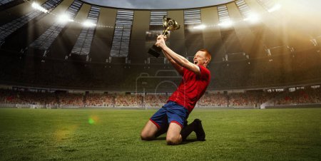Photo for Young happy man, professional sportsman in red uniform sitting on knees on 3D field with trophy after winning championship. Concept of sport, competition, game, emotions, success - Royalty Free Image