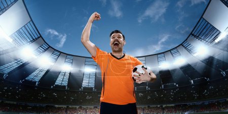 Photo for Man, professional football sportsman in orange uniform standing with winning look with ball on 3D field with spotlights. Successful championship. Concept of sport, competition, game, emotions - Royalty Free Image