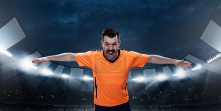 Photo for Growing winning spirit before game. Emotional man, professional sportsman in orange uniform standing on 3D field with spotlights. Concept of sport, competition, game, emotions, championship - Royalty Free Image