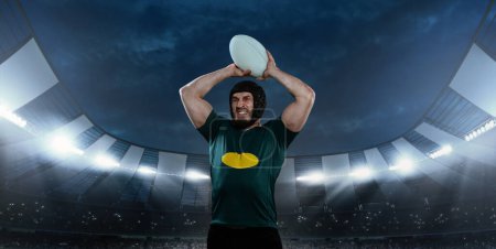 Photo for Man, professional rugby player in uniform standing with ball and emotional face at 3D stadium with flashlights. Game motivation. Concept of sport, competition, game, emotions, success - Royalty Free Image
