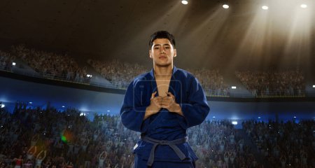 Photo for Young muscular man, professional martial arts sportsman, karateka in kimono standing with calm face on 3D field with spotlights. Concept of sport, competition, game, emotions - Royalty Free Image