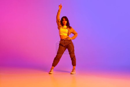 Photo for Beautiful young girl in sport style clothes dancing, making performance against gradient pink purple background in neon light. Concept of contemporary dance, youth, hobby, action and motion - Royalty Free Image