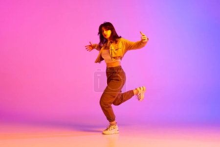 Foto de Imagen dinámica de una joven bailarina de ropa deportiva bailando sobre un fondo rosa púrpura degradado con luz de neón. Concepto de danza contemporánea, juventud, hobby, acción y movimiento - Imagen libre de derechos