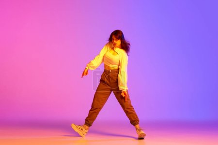 Photo for Young female dancer in sport style clothes making performance, training against gradient pink purple background in neon light. Concept of contemporary dance, youth, hobby, action and motion - Royalty Free Image
