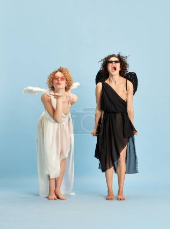 Kisses and anger. Cte, tender girl in image of angel and emotional shouting woman in image of devil against blue background. Concept of emotions, comparison of being, creativity, beauty