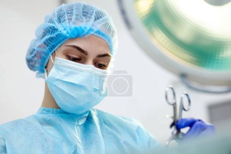 Photo for Close-up image of young woman, doctor, surgeon in protective medical mask leading surgery in medical clinic, hospital in surgery room. Concept of medicine, hospital, healthcare, treatment, profession - Royalty Free Image