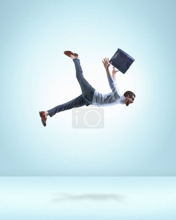 Photo for Motivated and ambitious young man, employee in formal wear with briefcase flying over light blue background. Professional growth. Concept of fantasy, inner world, dreams, surrealism, creativity - Royalty Free Image