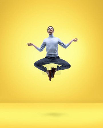 Photo for Staying calm and relaxed. Young man in classical clothes, employee levitating in lotus, yoga pose over yellow background. Concept of fantasy, inner world, dreams, surrealism, creativity, business - Royalty Free Image