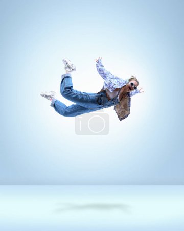Photo for Stylish young girl in casual clothes, headphones and sunglasses, flying over blue background. Imagination flow. Concept of fantasy, inner world, dreams, surrealism, creativity, youth, fashion - Royalty Free Image