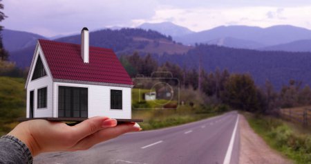 Photo for Changing places. Female hand holding 3D model of small house against round and mountains background. Concept of real estate, buying house, mortgage, ownership, business, property - Royalty Free Image