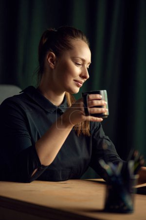 Photo for Portrait of beautiful, elegant business woman sitting at table, looking away and drinking coffee. Confidence and professionalism. Concept of business, , career development, profession, occupation - Royalty Free Image