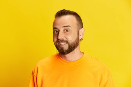 Photo for Portrait of young bearded man with short hair looking at camera, posing against vivid yellow background. Concept of human emotions, lifestyle, facial expression, fashion, sales, news. Ad - Royalty Free Image