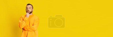 Photo for Portrait of bearded guy in casual sweatshirt posing with wide opened eyes, expressing schokc against vivid yellow background. Emotions, lifestyle, facial expression concept. Banner. Copy space for ad - Royalty Free Image
