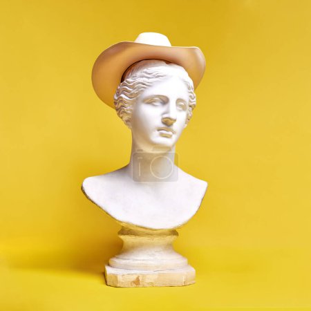 Téléchargez les photos : Buste de statue antique coiffé d'un chapeau sur fond jaune. Voyager, mode, style classique rétro. Concept de créativité, modernité et vintage, art antique. Inspiration et imagination - en image libre de droit