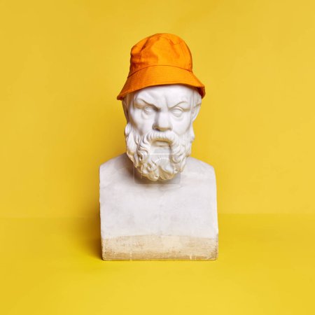 Foto de Busto de estatua antigua de hombre barbudo serio con panama naranja sobre fondo amarillo. Moda. Concepto de creatividad, modernidad y arte vintage, antiguo. Inspiración e imaginación - Imagen libre de derechos
