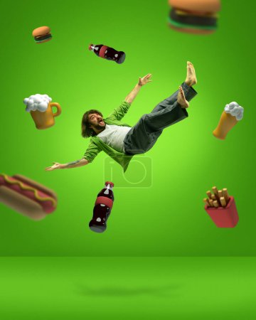 Foto de Comida prohibida. collage de arte contemporáneo con el hombre levitando y gritando entre la comida chatarra, cerveza, cola, papa francesa, sándwich, hot dog sobre fondo verde. Concepto de dieta, malos hábitos, adiposidad - Imagen libre de derechos