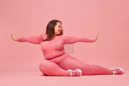 Photo for Well-being and self-love. Young overweight woman training in pink sportswear, doing stretching against pink studio background. Concept of sport, body-positivity, weight loss, body and health care - Royalty Free Image