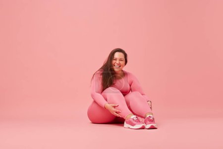 Self-care and well being. Young overweight woman training in sportswear against pink studio background. Laughing. Concept of sport, body-positivity, weight loss, body and health care