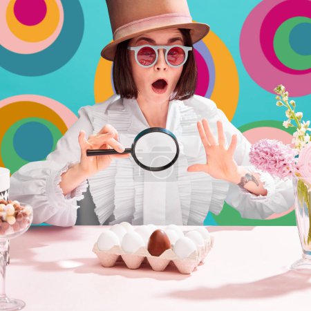 Téléchargez les photos : Femme choquée dans des lunettes de soleil et chapeau cylindre regardant émotionnellement dans la loupe aux œufs en chocolat parmi ordinaire. Fond abstrait multicolore. Concept de pop art, créativité, gastronomie, vacances - en image libre de droit