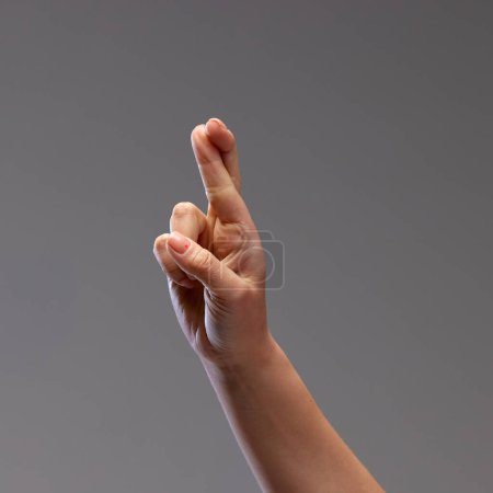 Foto de Mano masculina cruzando dedos, mostrando gesto de buena suerte sobre fondo gris. Esperando el bien y el éxito. Concepto de relación humana, comunidad, simbolismo, cultura, comunicación - Imagen libre de derechos