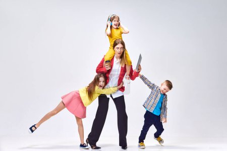 Photo for Multitasking. Work and parenting. Portrait woman and playful, noisy little kids posing against grey studio background. Concept of family, motherhood, childhood, fashion, lifestyle, work - Royalty Free Image