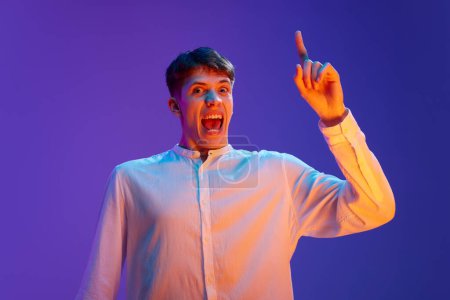 Photo for Portrait of young emotional man in white short raising finger, paying attention against gradient purple background in neon light. Information. Concept of human emotions, lifestyle, youth - Royalty Free Image