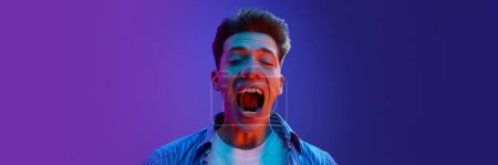 Photo for Portrait of young emotive man guy in casual clothes showing success and winning look, excitement on gradient purple background in neon light. Concept of human emotions, lifestyle. Copy space for ad - Royalty Free Image