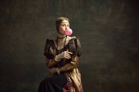 Téléchargez les photos : Portrait de jolie jeune fille, princesse médiévale en robe vintage posant avec chewing-gum sur fond vert foncé. Concept d'histoire, remake de l'art de la renaissance, comparaison des époques, modernité - en image libre de droit