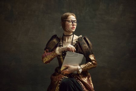 Photo for Portrait of young, pretty girl, royal person in vintage dress and modern glasses posing with laptop against dark green background. Business woman. History, renaissance art, comparison of eras concept - Royalty Free Image