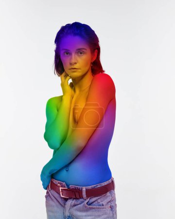 Foto de Retrato de mujer joven de pie sin camisa con el cuerpo coloreado en colores del arco iris, simbolizando la aceptación lgbt sobre fondo blanco. Concepto de comunidad lgbt, apoyo, amor, derechos humanos, mes del orgullo - Imagen libre de derechos