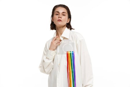 Foto de Retrato de mujer joven en camisa blanca con línea de arco iris que simboliza el apoyo lgbt, saliendo. Modelo posando sobre fondo blanco. Concepto de comunidad lgbt, apoyo, amor, derechos humanos, mes del orgullo - Imagen libre de derechos