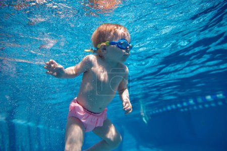 Foto de Qué mirada más graciosa. Niña, niño pequeño en traje de baño rosa y gafas nadando bajo el agua en la piscina. Deportes acuáticos. Concepto de deporte, estilo de vida saludable y activo, infancia, diversión y entrenamiento - Imagen libre de derechos