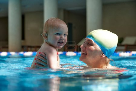 Photo for Happy mother, smiling, holding cute with little kid, girl, daughter in swimming pool indoors on warm sunny day. Concept of sport, healthy and active lifestyle, childhood, fun and training - Royalty Free Image