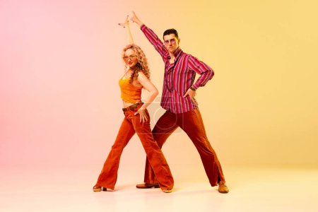 Téléchargez les photos : Artistique, expressif homme et femme dans des vêtements élégants dansant disco, danse rétro sur fond rose jaune dégradé. Concept de style rétro, danse, mode, art, passe-temps, musique, années 70, passe-temps - en image libre de droit