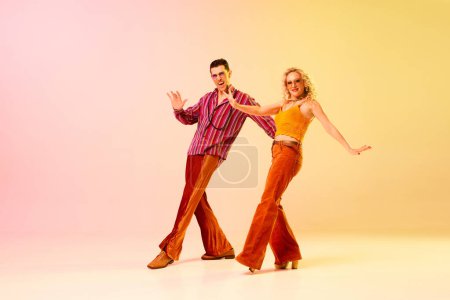 Photo for Expressive, talented, emotional couple, man and woman in stylish clothes dancing disco dance against gradient pink yellow background. Concept of retro style, dance, fashion, art, hobby, music, 70s - Royalty Free Image