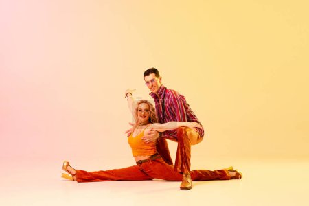 Photo for On twine. Support. Expressie, talented young couple, man and woman in vintage clothes dancing against gradient pink yellow background. Concept of retro style, dance, fashion, art, hobby, music, 70s - Royalty Free Image