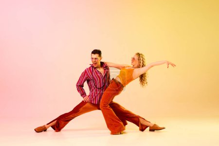 Aufregung. Künstlerisches, ausdrucksstarkes Paar, Mann und Frau tanzen gefühlvoll Disco-Tanz vor rosa-gelbem Hintergrund. Konzept des Retro-Stils, Tanz, Mode, Kunst, Hobby, Musik, 70er Jahre