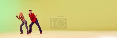 Téléchargez les photos : Beau, homme émotionnel et femme dans des vêtements rétro élégants dansant sur fond jaune vert dégradé. Concept de style rétro, danse, mode, art, passe-temps, musique, années 70. Bannière. Espace de copie pour la publicité - en image libre de droit