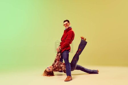Photo for Retro party. Emotional expressive young man and woman in vintage style outfits dancing against gradient green yellow background. Concept of retro style, disco dance, fashion, art, hobby, music, 70s - Royalty Free Image