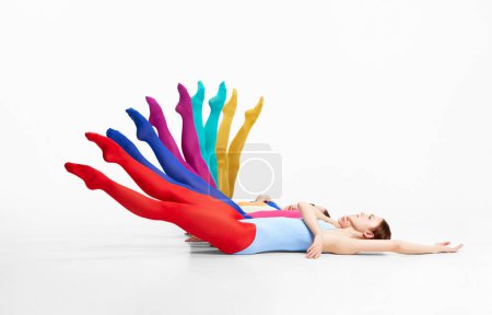 Photo for Rainbow. Group of young girls in bright tights lying on floor, raising legs, dancing against grey studio background. Concept of beauty, creativity, classic dance style, elegance, contemporary art - Royalty Free Image