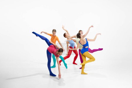Foto de Grupo de bailarinas artísticas de ballet en ropas brillantes y multicolores actuando, bailando sobre fondo gris del estudio. Concepto de belleza, creatividad, danza clásica, elegancia, arte contemporáneo - Imagen libre de derechos