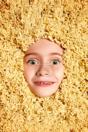 Photo for Funny image with cute face of beautiful little girl, child peeking out noodles background. Fun, food, nutrition, fantasy. Concept of childhood, emotions, fun, fashion, lifestyle - Royalty Free Image