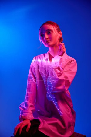 Foto de Ternura. Retrato de niña en blusa blanca con reflejo de filtro de neón posando sobre fondo azul en luces de neón. Concepto de arte, estilo moderno, cyberpunk, futurismo y creatividad - Imagen libre de derechos